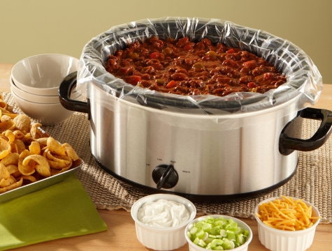 Slow cooker with a liner and chili inside surrounded by small bowls of toppings