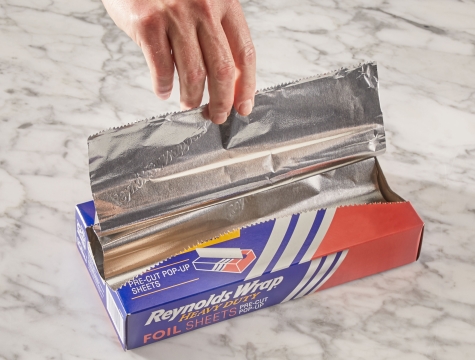 Person pulling a sheet of aluminum foil from a box