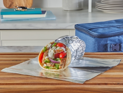 Gyro sandwich wrapped in foil sitting on a kitchen counter next to a lunchbox