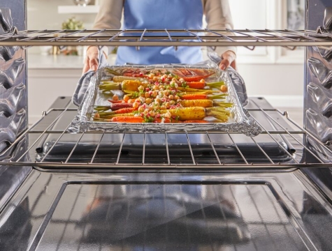 Person removing roasted vegetables on a foil lined pan from the oven