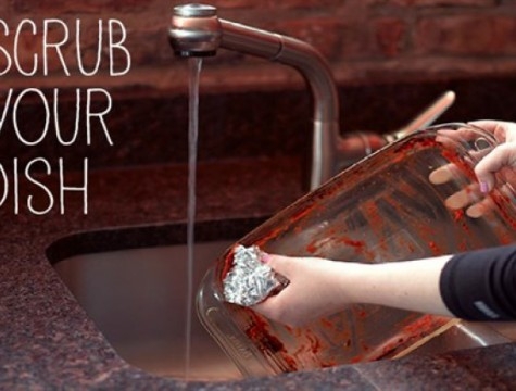 person scrubbing a glass casserole dish with a ball of aluminum foil