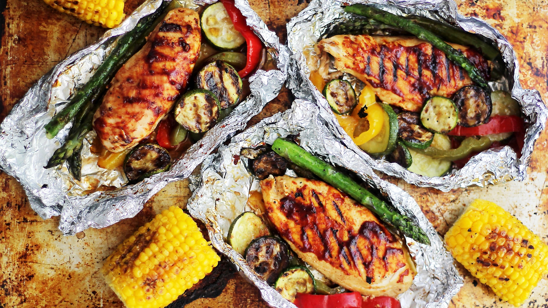 Grilled chicken and vegetables sitting in foil packets