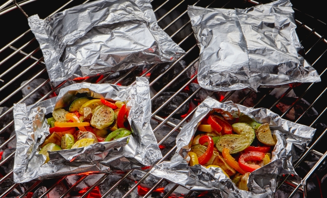 Foil packets with roasted vegetables sitting on a charcoal grill
