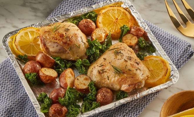 Baking sheet covered in aluminum foil and topped with roasted chicken, potatoes, spinach and lemons