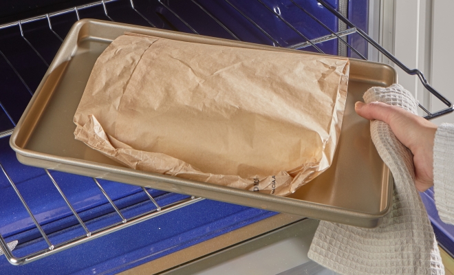 person removing a sealed parchment cooking bag from the oven