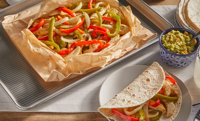 chicken fajitas sitting in an open parchment cooking bag alongside a fajita wrapped in a tortilla