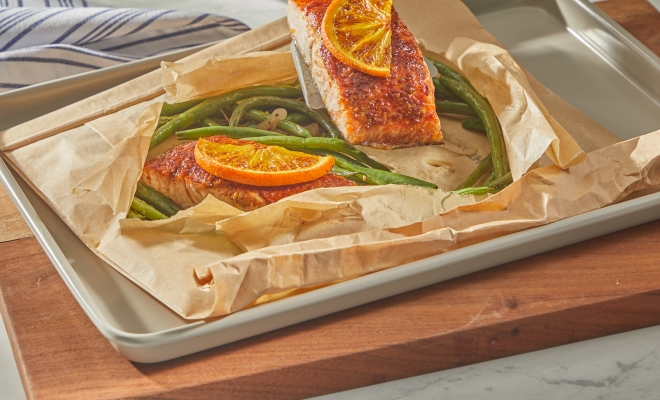 person lifting a salmon filet from an open parchment cooking bag