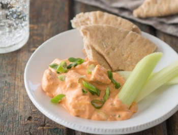 Buffalo chicken dip on a plate alongside pita bread and celery sticks