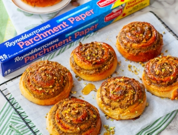 Pistachio Honey Cinnamon Rolls sitting on a sheet of Reynolds parchment paper on a wire cooling rack