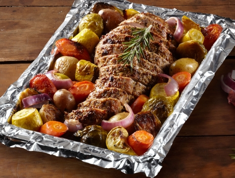 Sliced pork tenderloin surrounded by diced potatoes, carrots and onions on an aluminum foil lined baking sheet