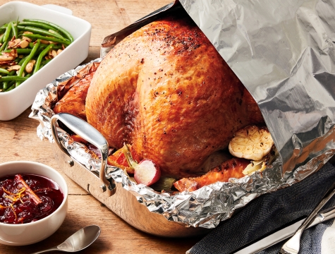 Roasted turkey sitting in a foil lined roasting pan covered with an aluminum foil tent
