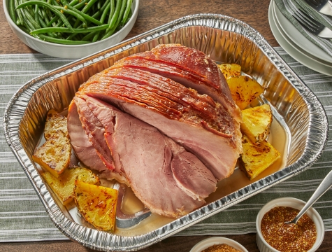 Spiral ham sitting in a disposable roasting pan surrounded by chunks of pineapple